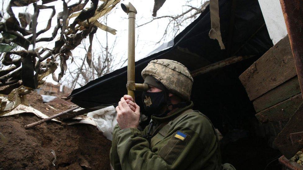 Ukrainian soldier looking through a telescope stood in a trench