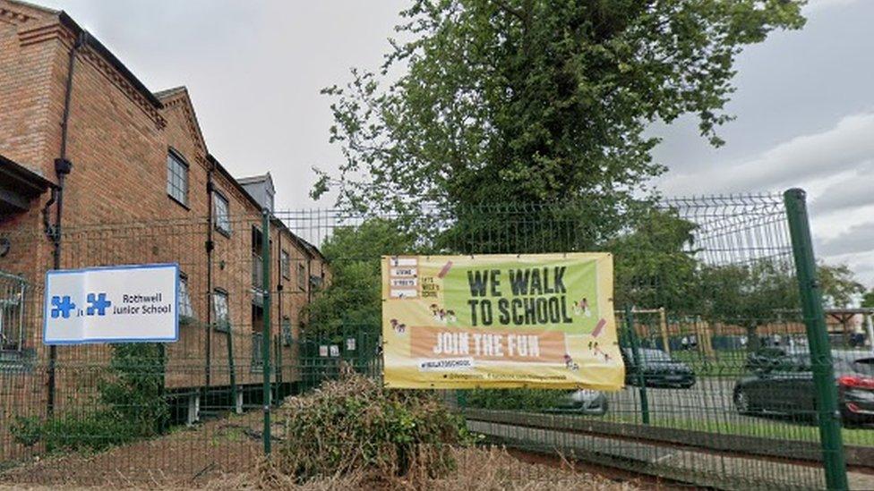 School sign on a railing outside a classroom building, The car park is also visible.