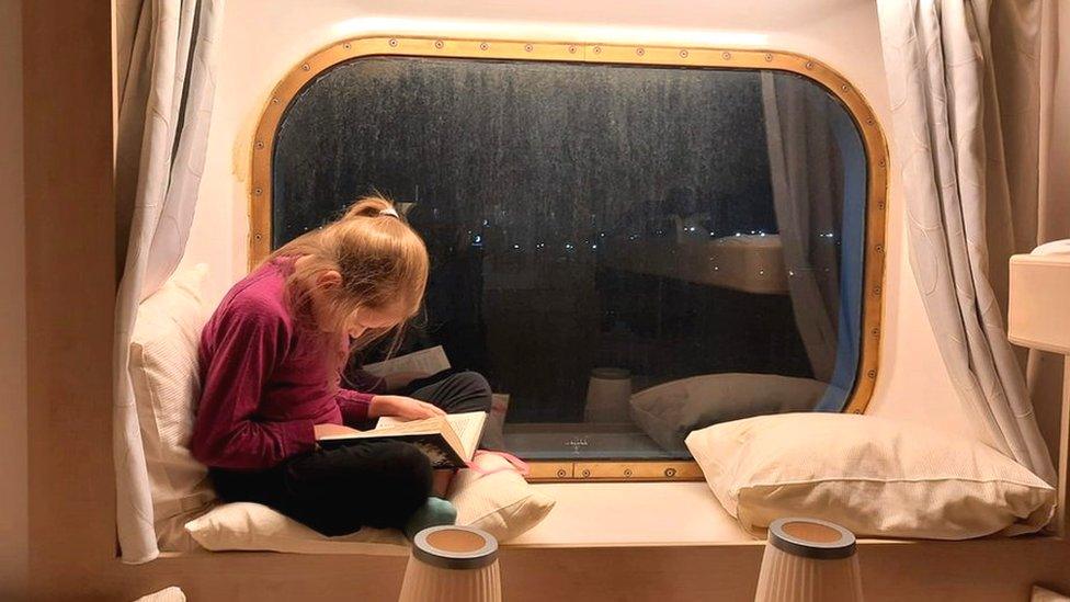 Polina reads in the window of her room on the cruise ship