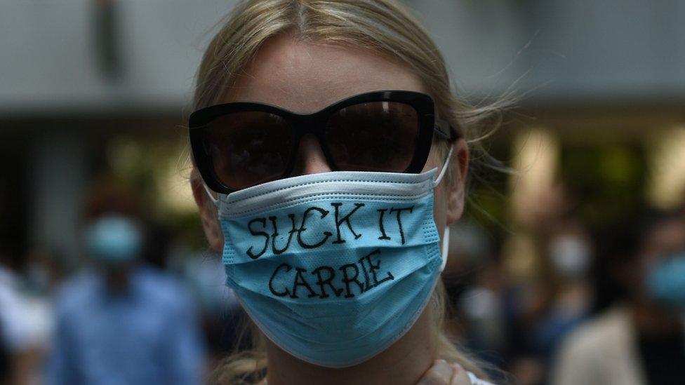 A pro-democracy demonstrator wears a mask that reads "suck it Carrie" as she and others gather at Chater Garden