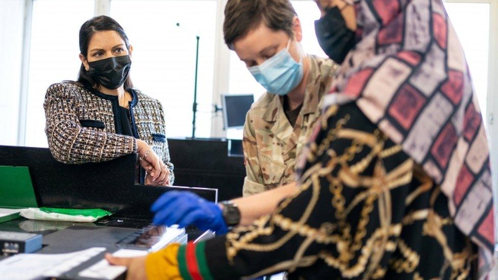 A woman is registered and her fingerprints taken as the Home Secretary looks on