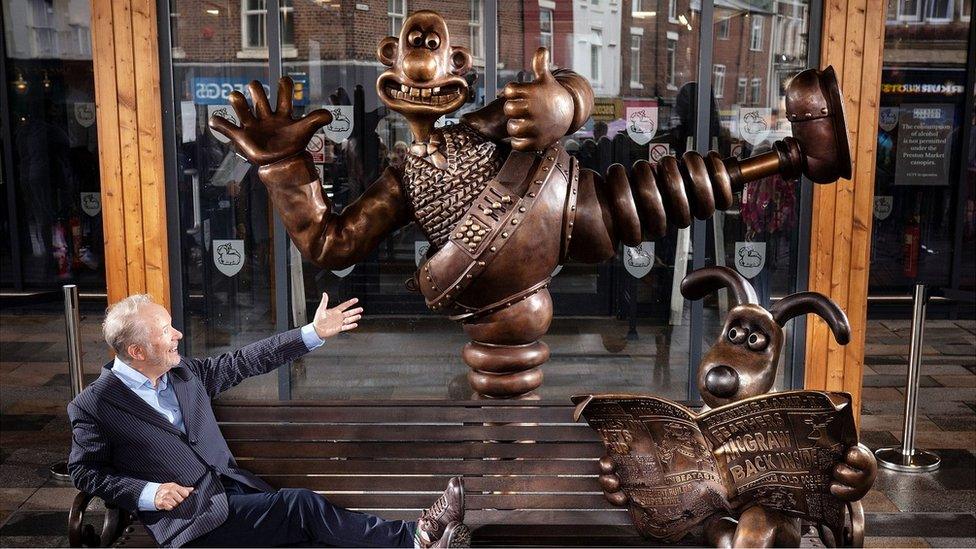 Nick Park poses on bench with Wallace and Gromit statue
