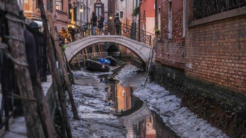 riverbanks exposed in venice canal with bridge in background