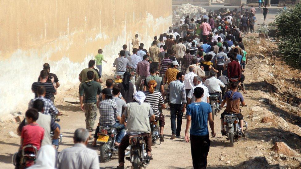 Syrians walk and ride motorcycles during the funeral of seven members of the Syrian civil defence volunteers, also known as the White Helmets, during their funeral in Sarmeen