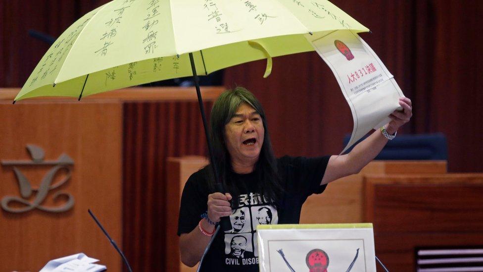 Newly elected pro-democracy lawmaker Leung Kwok-hung, known as "Long Hair," holds a yellow umbrella and a oversized mock copy of controversial, proposed anti-subversion legislation as she takes the oath in the new legislature Council in Hong Kong, Wednesday, Oct. 12, 2016