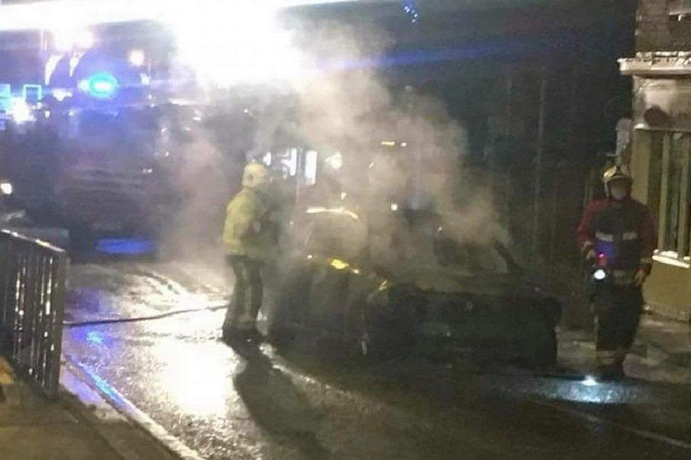 Firefighters next to smouldering car