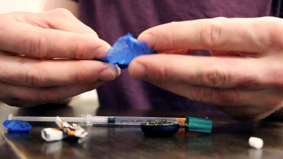 Elliot removing drugs from a blue bag