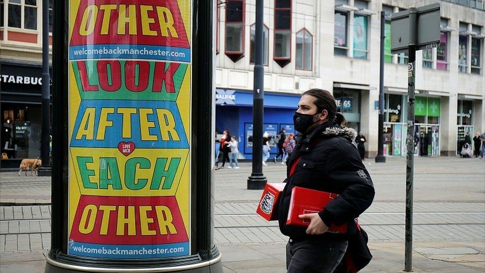 Person in mask in front of sign reading 'Look after each other' in Manchester