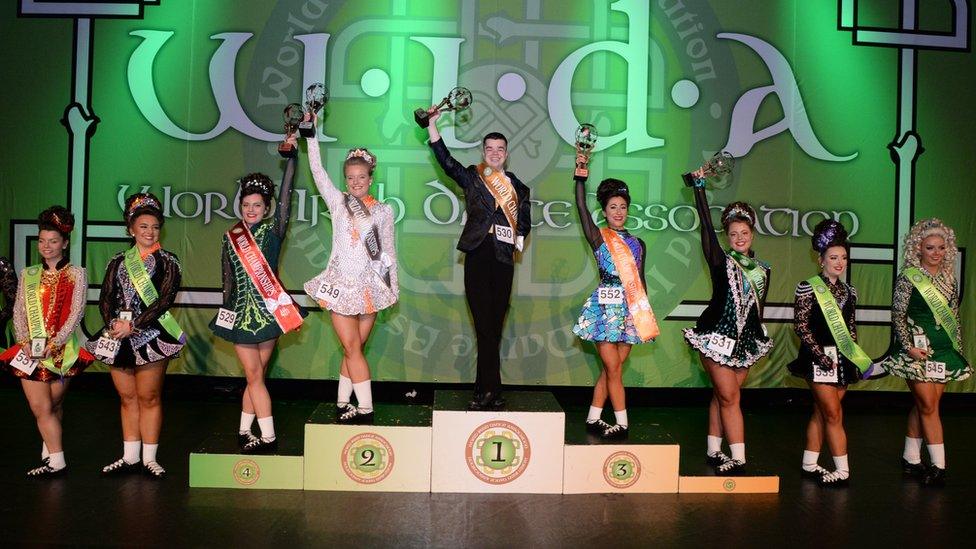 Irish dancers standing on podiums whileholding trophies in the air