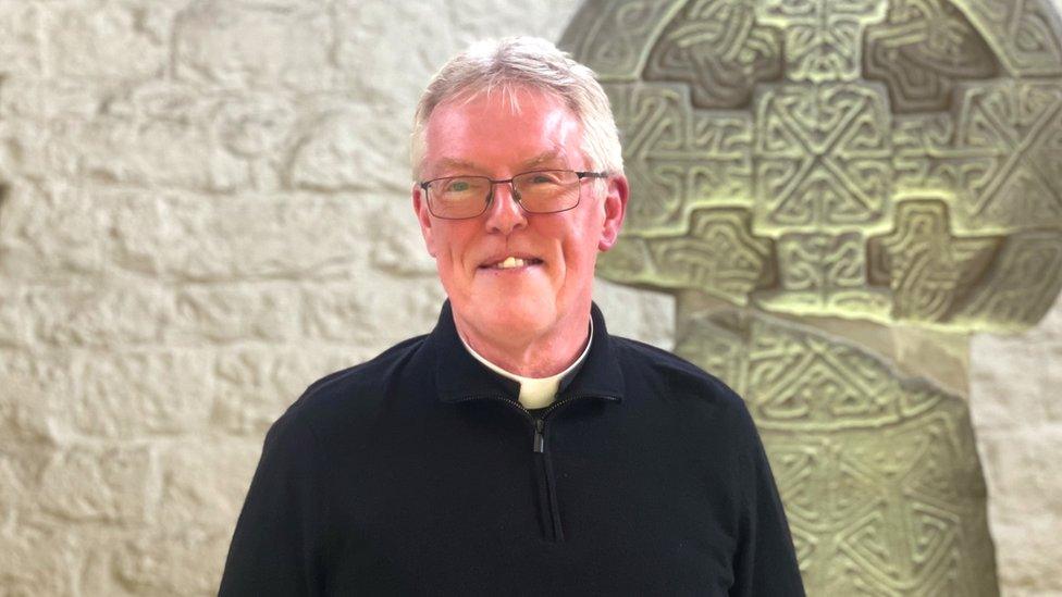 Father Edwin Counsell standing in front of St Illtud's Celtic standing stones