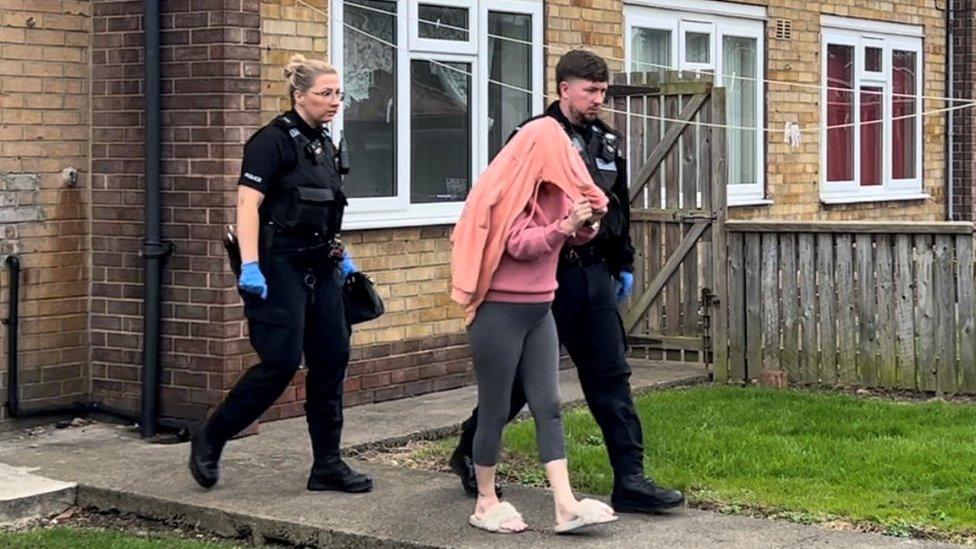 A woman hidden under a jumper, escorted by police