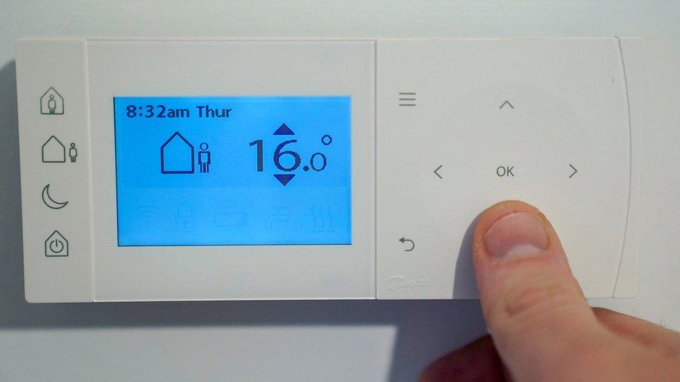 A homeowner turning down the temperature of a central heating thermostat