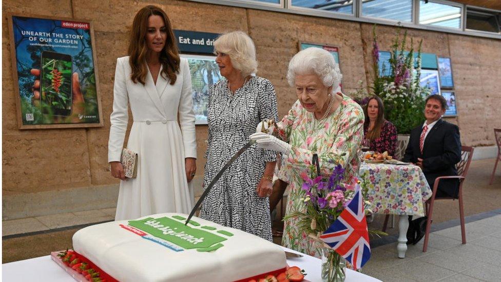 The Queen, Duchess of Cambridge and Duchess of Cornwall cut a cake with a sword.