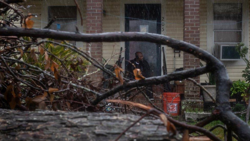 A man waits for the arrival of Hurricane Delta, surrounded by debris that was blown into his garden by Hurricane Laura