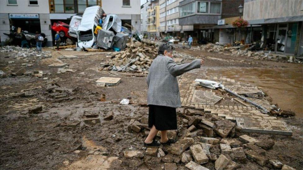 An old woman cleans up rubbish from a destroyed building