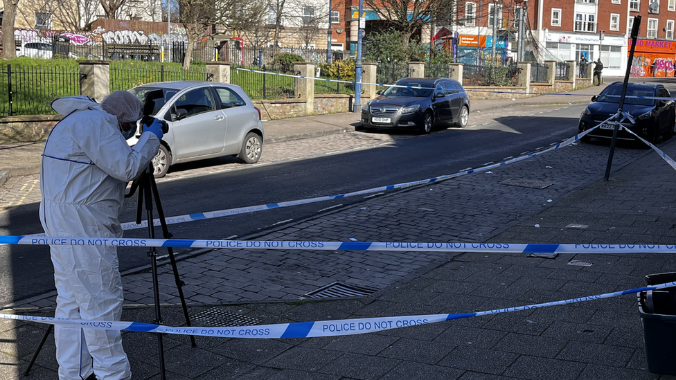 Police forensic teams photograph a street within a police tape cordon in Bristol