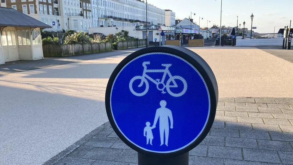 A cycling and pedestrian blue sign in front of the plaza