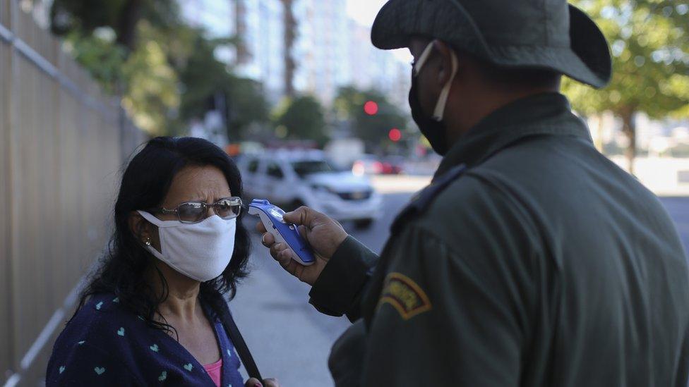 A member of the Municipal Civil Guard checks the temperature of a pedestrian in Brazil