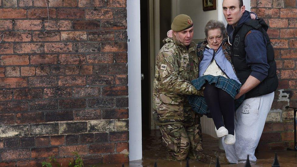 An elderly woman is carried from her home by two men