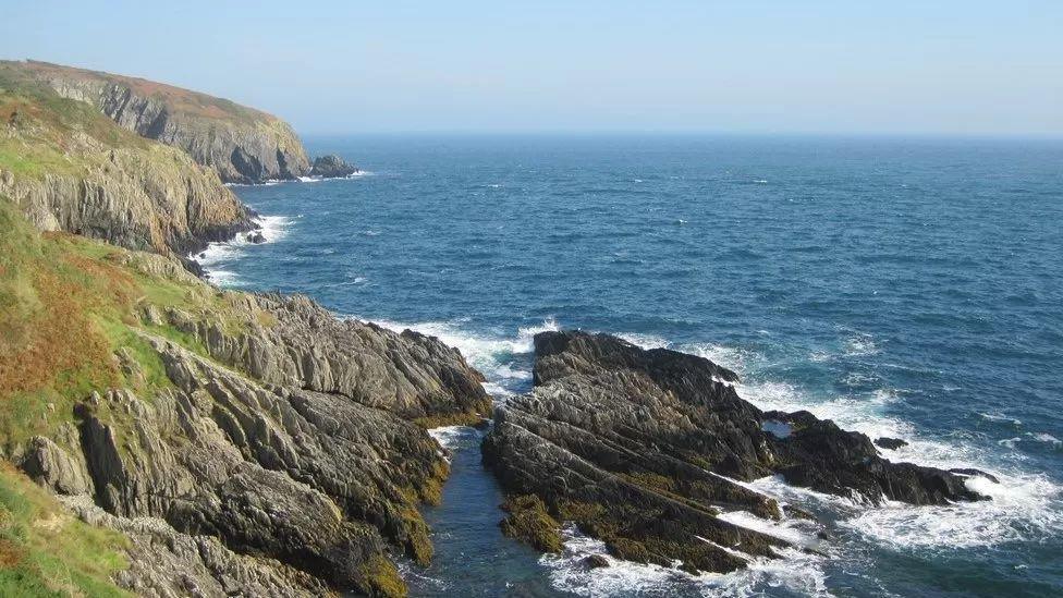 The rugged coastline near Maughould rocks stick out of the sea, and you can see grass on the cliffs.