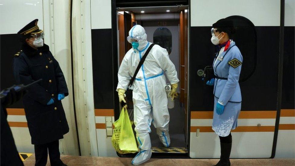 A worker in full protective equipment steps off a train in the Olympics closed-loop area.