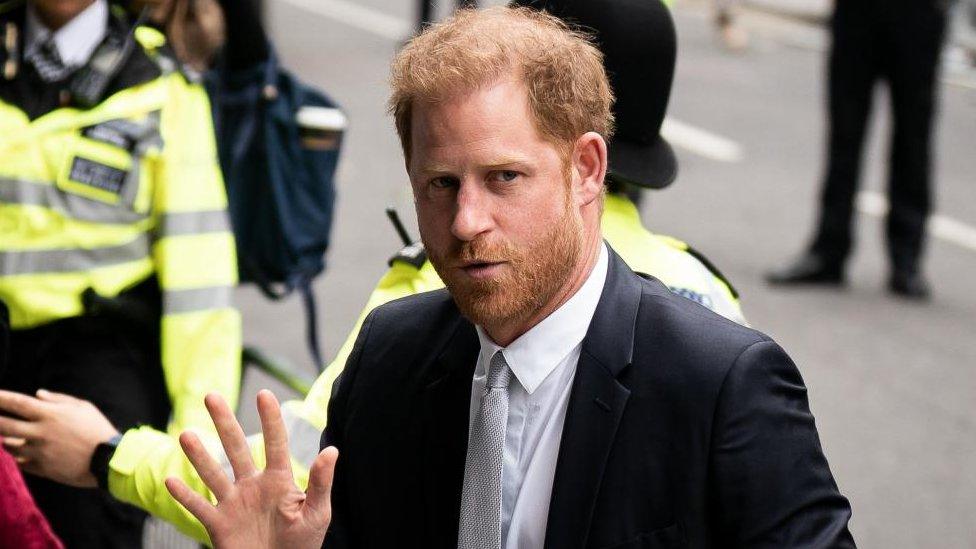 Prince Harry waving to reporters as he arrives at court