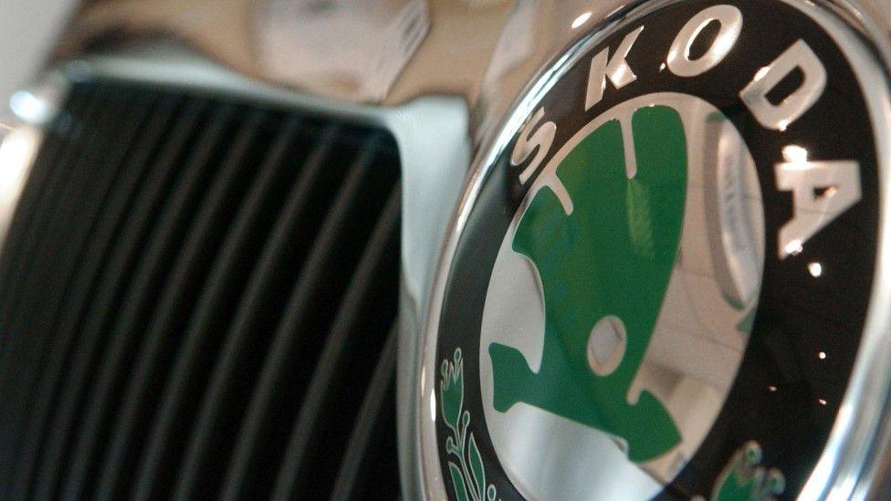 Close-up shot of a green and Skoda badge on the front grill of a car. 