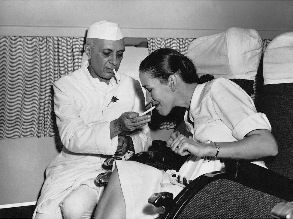 Mr Nehru lights a cigarette for the wife of a British diplomat while on board the first BOAC or round-the-world flight in India.