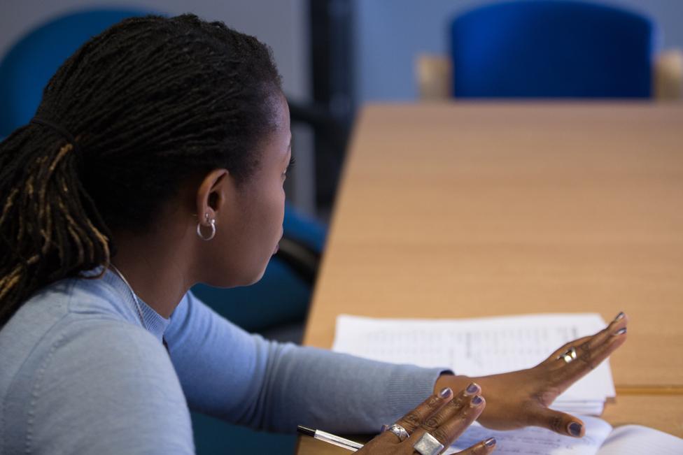 Woman member of staff talks while seated at table