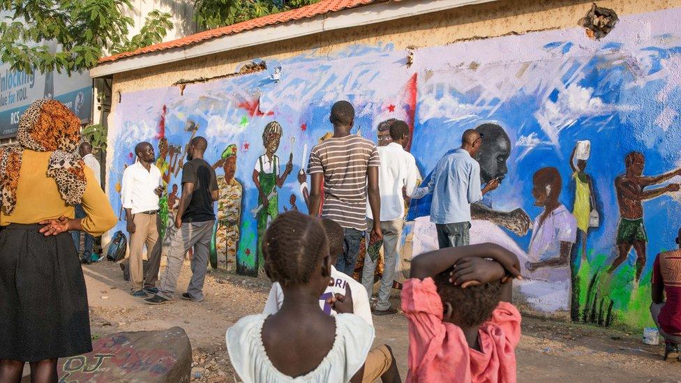 People gather round a mural depicting various different figures in society, eg doctors, soldiers and mechanics.