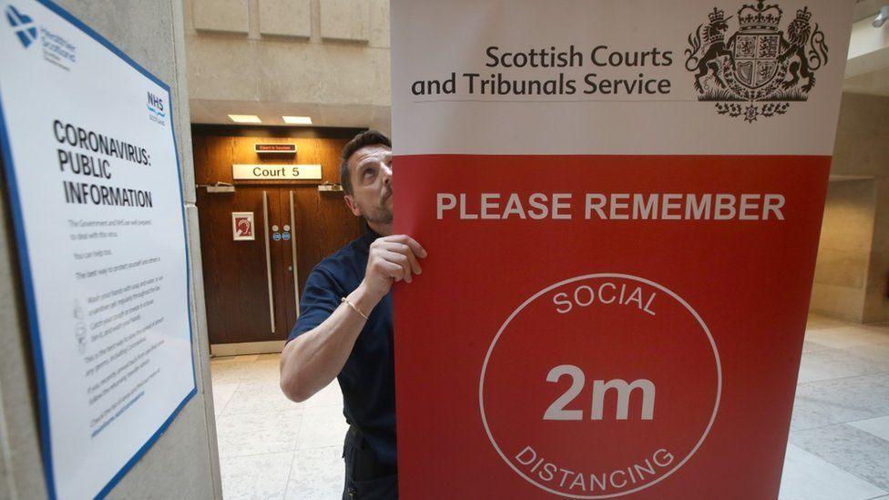 A man erects a social distancing sign outside a Scottish court during the Covid pandemic