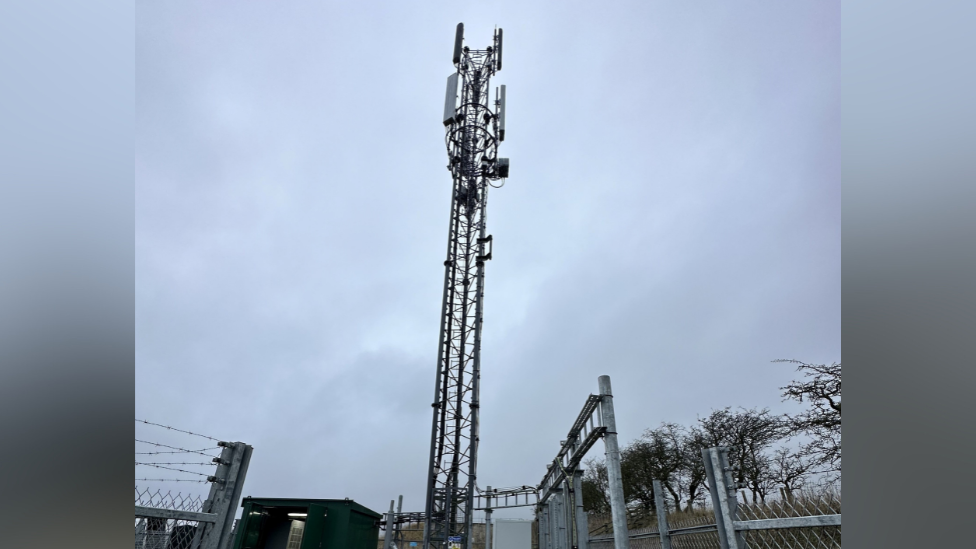 The mast tower with fencing around it on a cloudy day.