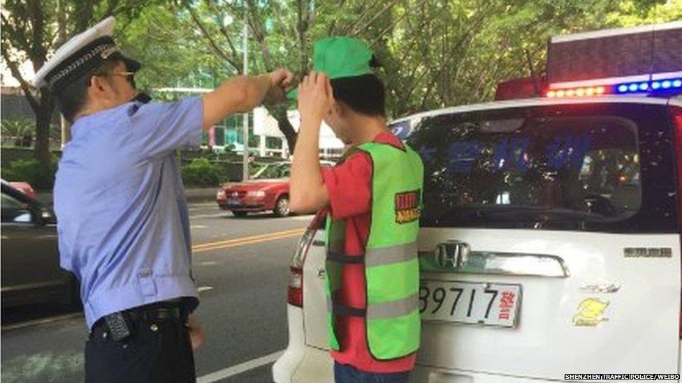 A police officer puts a green cap on a pedestrian who is also wearing a green vest