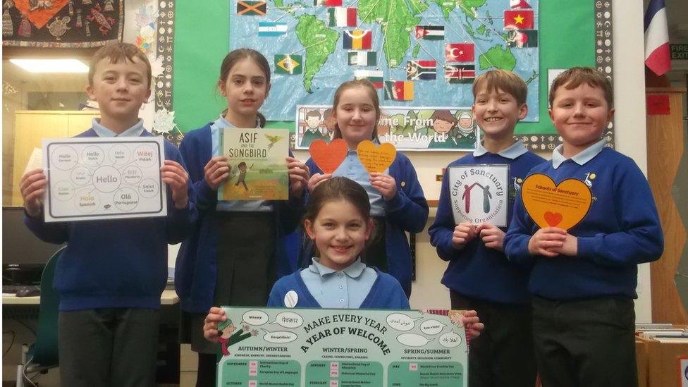 Six children from Peatmoor Primary school's welcoming committee in front of a map of the world