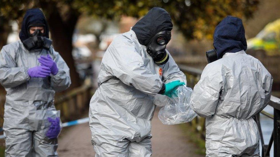 Police officers in protective suits and masks work near the scene