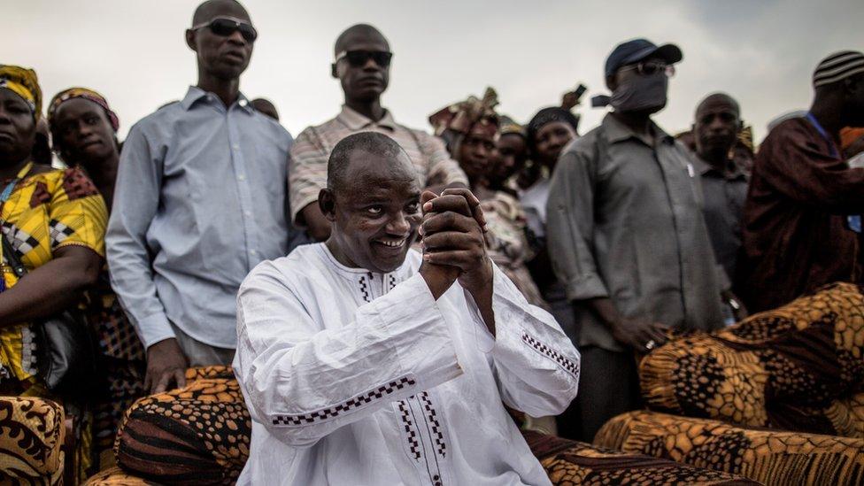 Adama Barrow greets people while sitting.