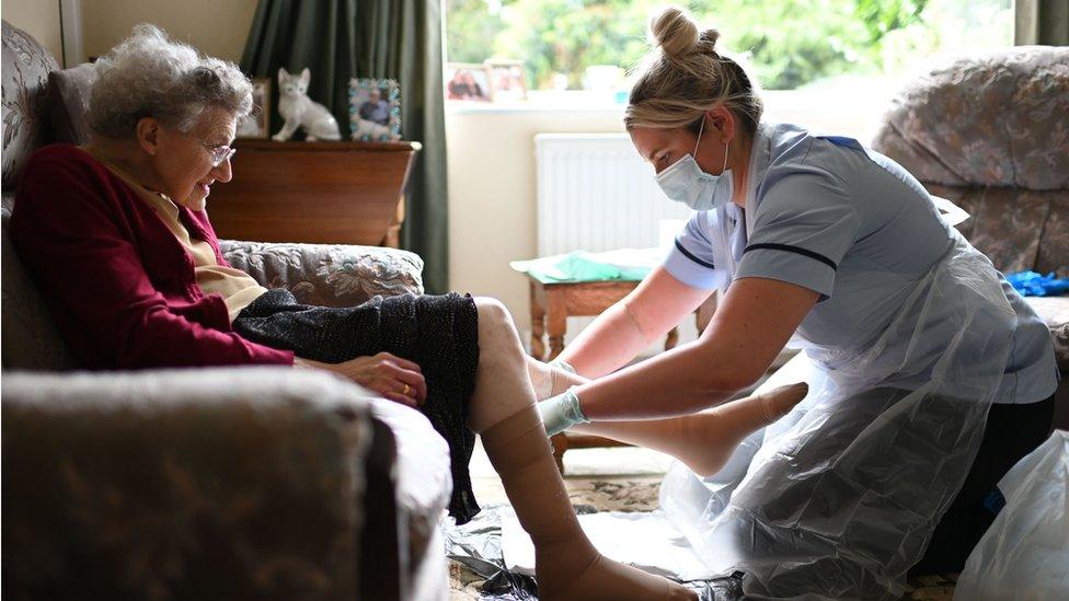 A care worker helps a care home resident put stockings on