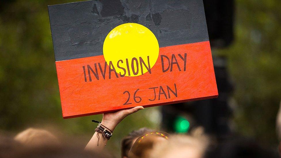 A protester holds a message written on an Aboriginal flag saying: "Invasion Day 26 Jan"