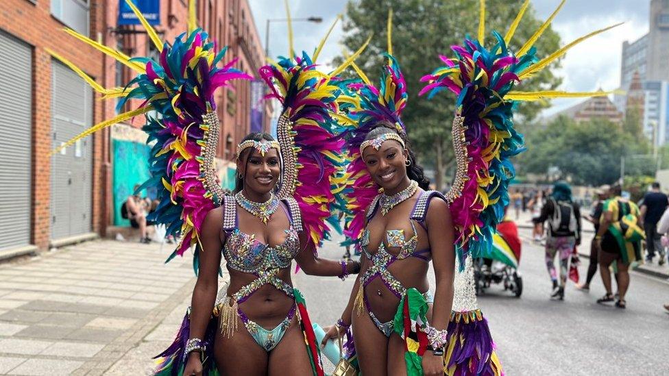 Two dancers with vibrant feathers head to their floats