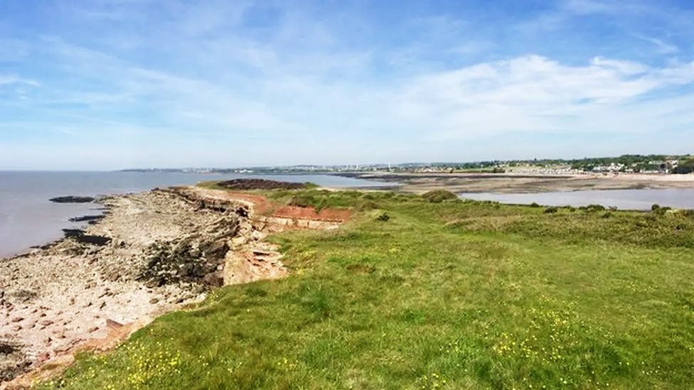 Llun o lwybr cul gyda gwair sydd wedi ei gysyllltu a'r tir mawr. Mae dwr y mor bob ochr i'r llwybr