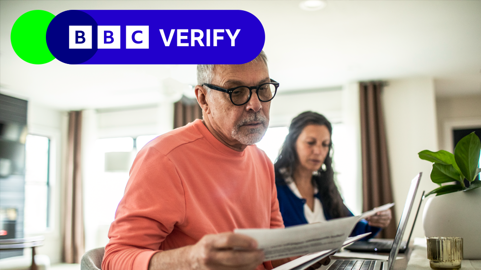 A stock photo shows a couple looking at bills at home, with the BBC Verify logo in the top left hand corner of the image.