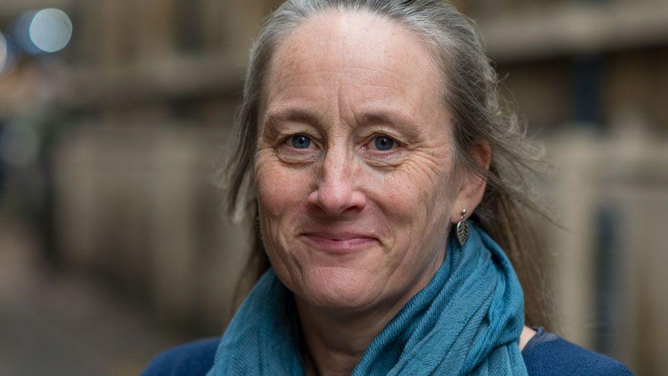 Prof Alice Reid wearing a lighter blue scarf and a mid blue top looking at the camera