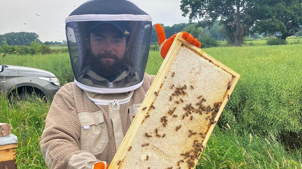 Nathan Egerton Evans in a bee keepers suit holding a beehive