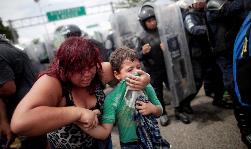 A woman covers her young son's mouth with his tshirt. Tear gas was fired by Mexican police as they tried to force back the crowd.