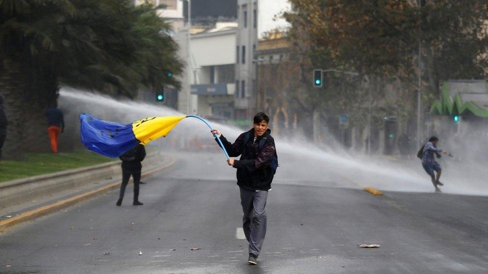 A demonstrator waves a flag as they clash with riot police in Santiago