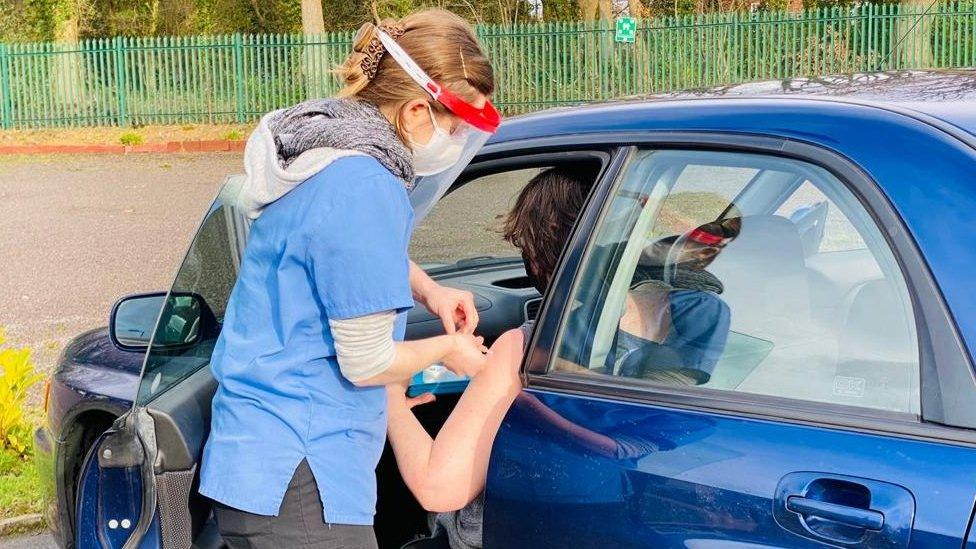 A nurse vaccinates someone through a car window