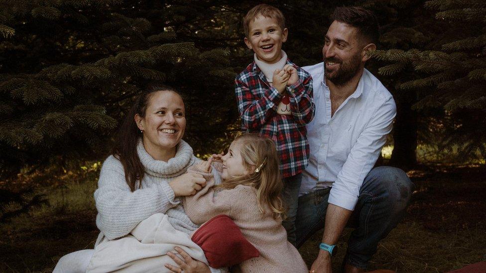 Karen and James Marks sitting on the ground with their three young children, all smiling