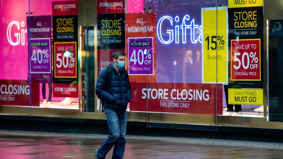 A man wearing a face mask passes "closing down" signs in the window of Debenhams, on Oxford Street, London.