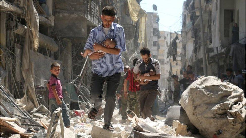 Syrian men carry babies through rubble in Salihin neighbourhood of Aleppo (September 2016)