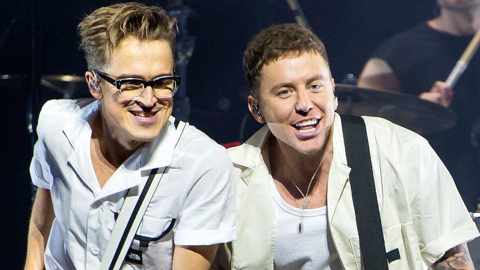 Tom Fletcher (L) in a white short-sleeved shirt, and Danny Jones, in a cream short-sleeved shirt over a white vest, of McFly perform at The O2 Arena on November 21, 2021 in London, England